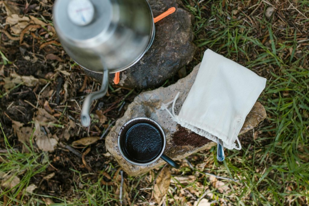 Top view of camping coffee setup with a brewed cup, kettle, and pouch outdoors.